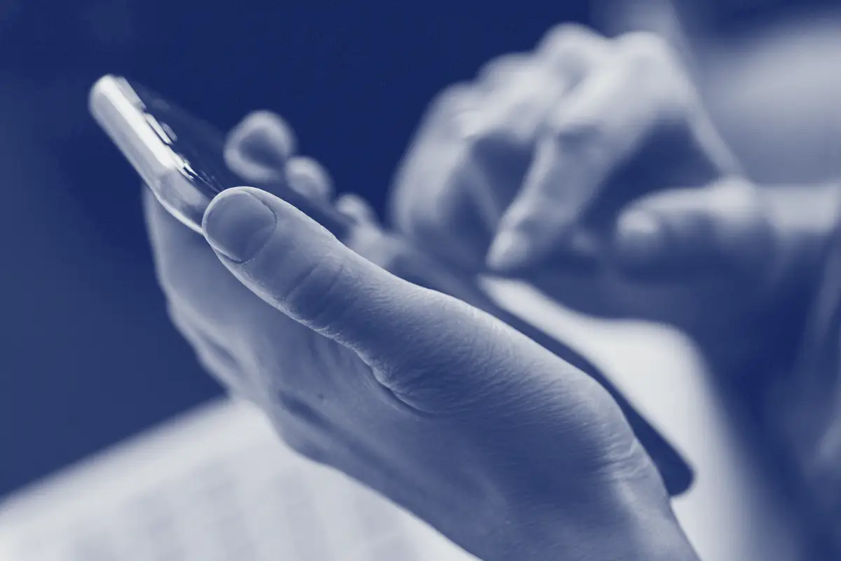 Hands holding a phone above a laptop keyboard