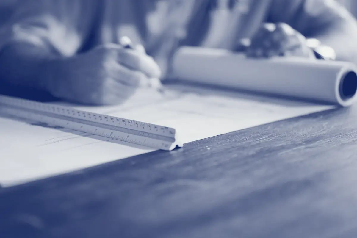 A hand drafting a plan with a pencil and scale ruler